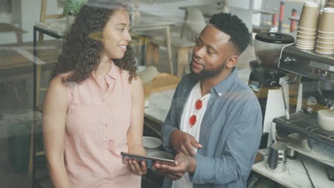 happy african american male cofe owner and biracial female barista using smartphone and talking