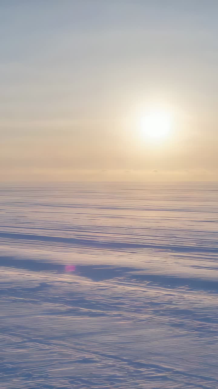 Vertical video: Filming camera showing snow plain on ice, sun glare shifting and lens flare moving