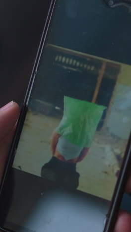 man watches video of girlfriend kidnapping victim with bag on head via mobile phone and blows smoke near laptop in semi-dark room closeup slow motion