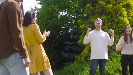 Side-view-of-caucasian-young-woman-throwing-a-petanque-ball-in-the-park-on-a-sunny-day-while-her-friends-waiting-their-turns