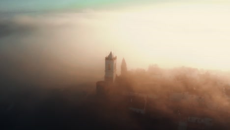 desolate medieval town and castle tower jutting out through heavy fog at sunrise