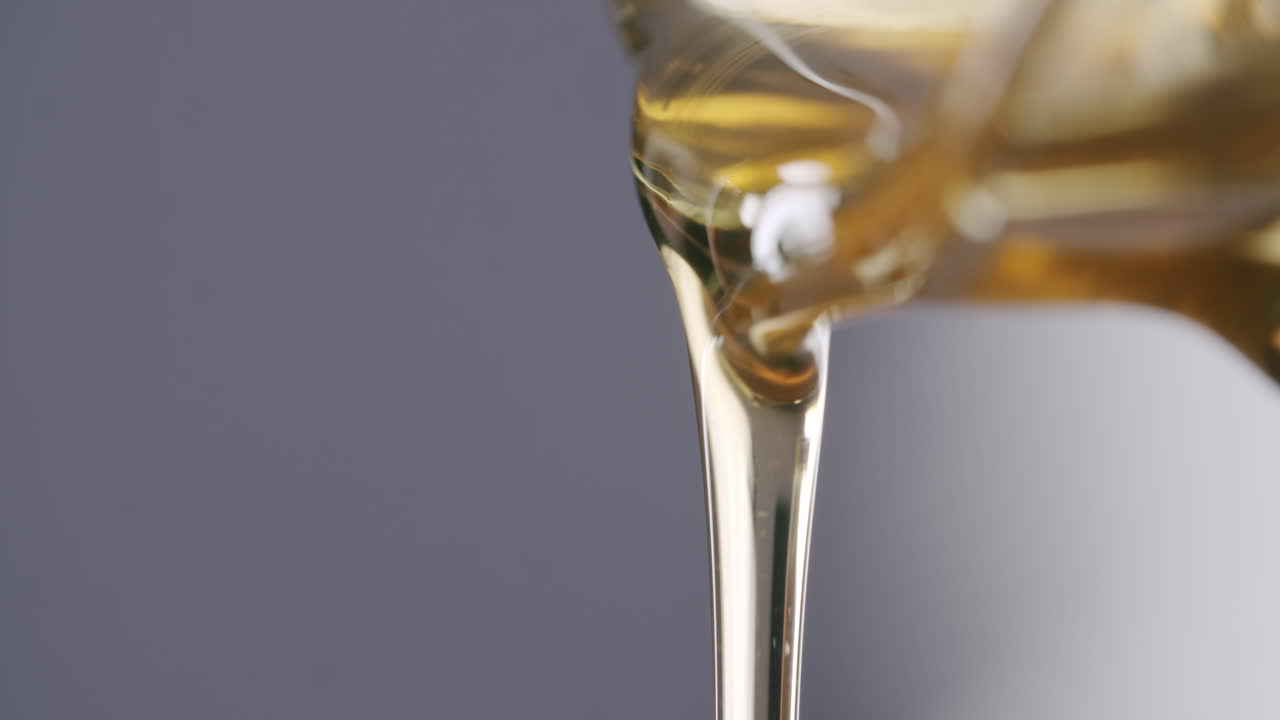 Macro close up shot of viscous honey flowing out of a honey jar before a grey studio background