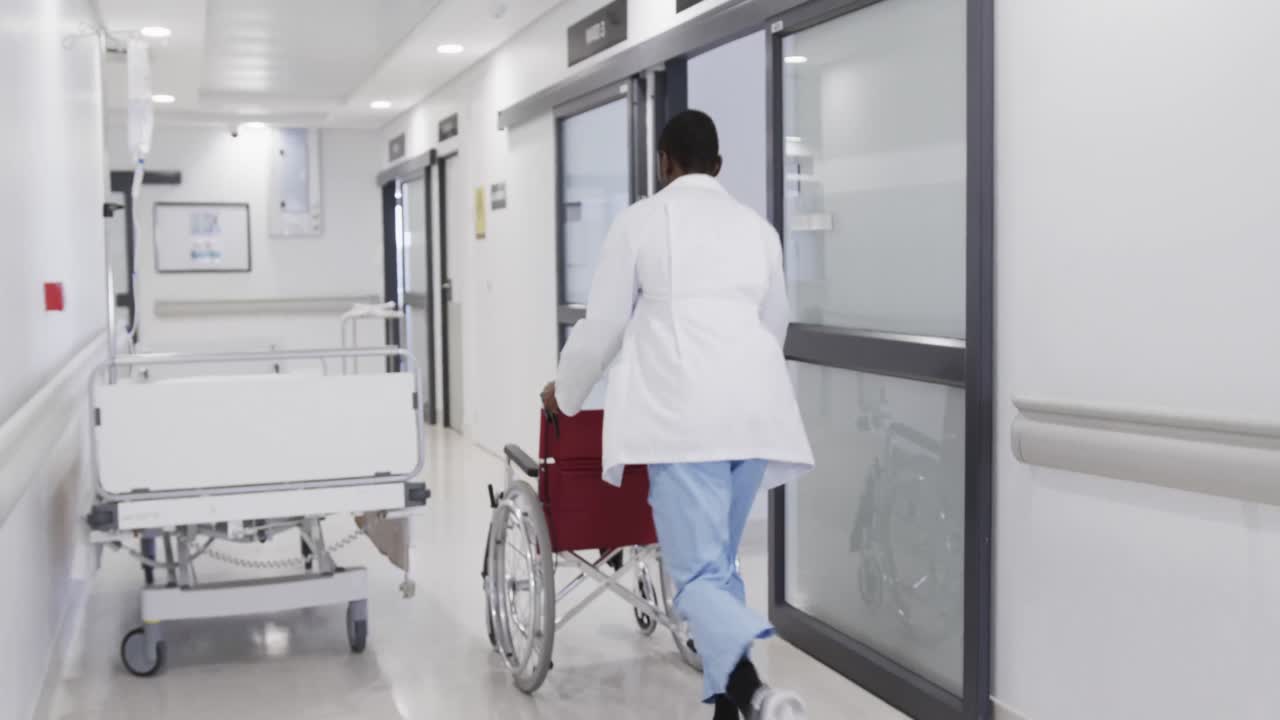 Afroamerikansk mandlig læge løber med kørestol på hospitalsgang, i slowmotion