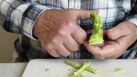 closeup of male hands peeling broccoli stems over a cutting board while sitting on a table.