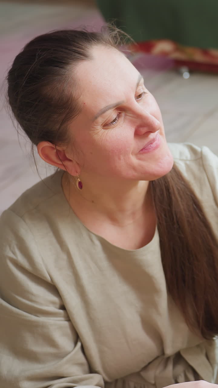 Una mujer caucásica en un salón acogedor, con una mirada apacible, suave luz matutina, una sonrisa dulce y pelo castaño largo sobre el hombro, un jersey cómodo y un sofá de fondo, un primer plano íntimo que transmite una calma contemplativa