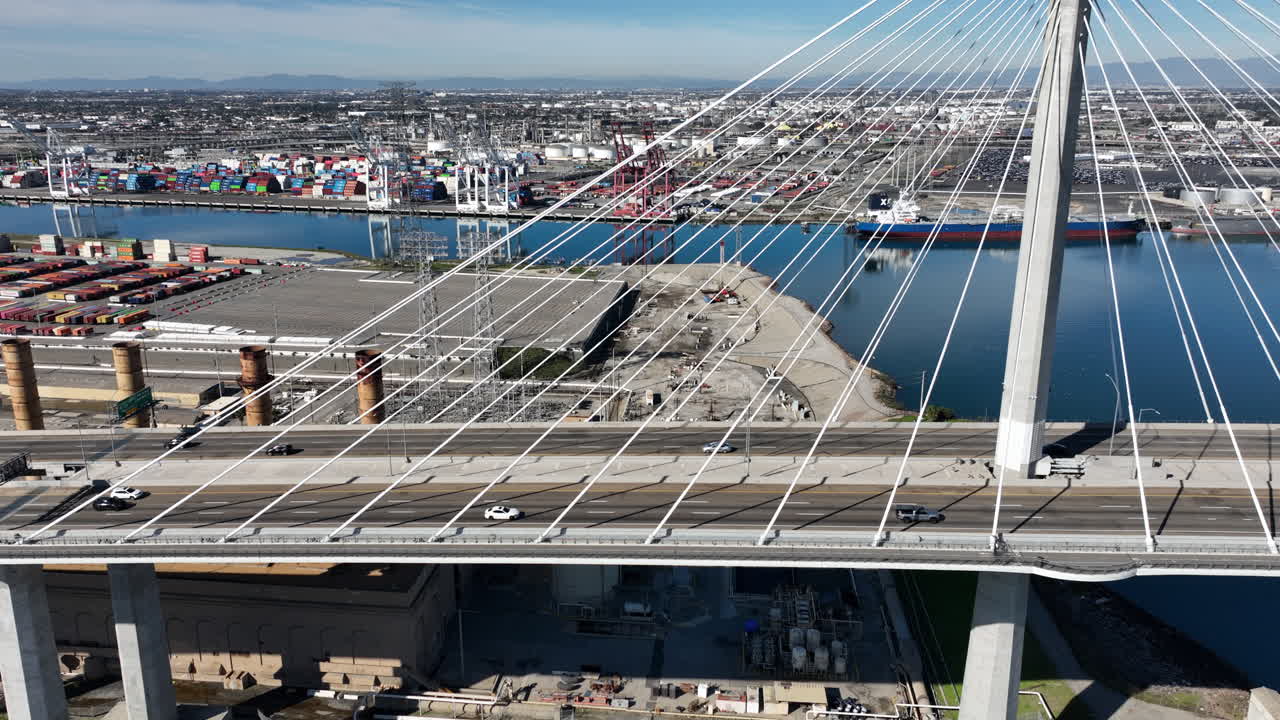 Aerial view of the International Gateway Bridge in Long Beach, California next to Terminal Island, with shipping containers, 18-wheelers, and the Port of Los Angeles visible