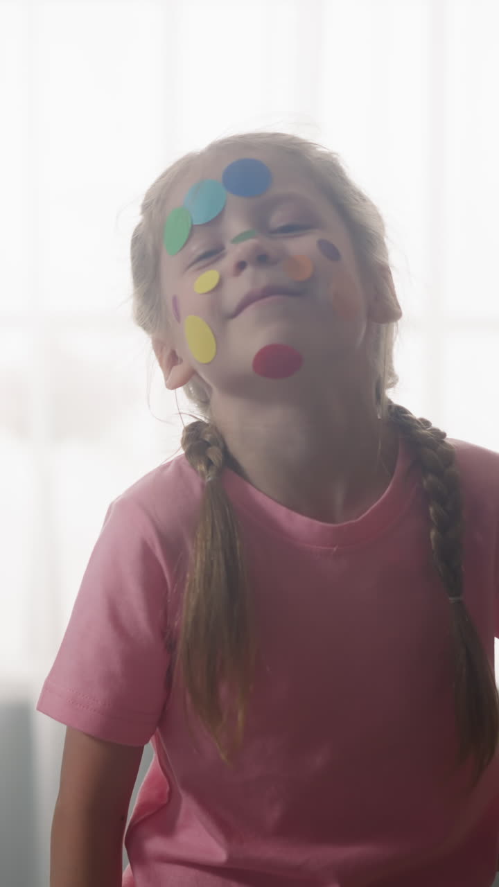 Little brother and elder sister with polka dot stickers on faces stand against bright window in room slow motion. Funny children party. Art and creativity
