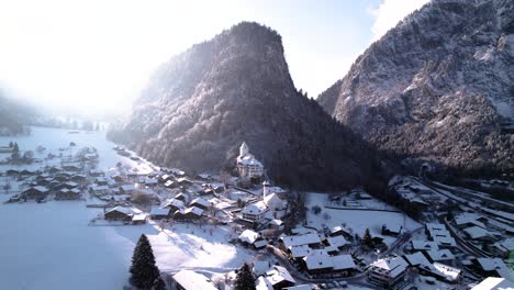 vista aérea de un pueblo de montaña con una iglesia y montañas cubiertas de nieve en suiza en un soleado día de invierno