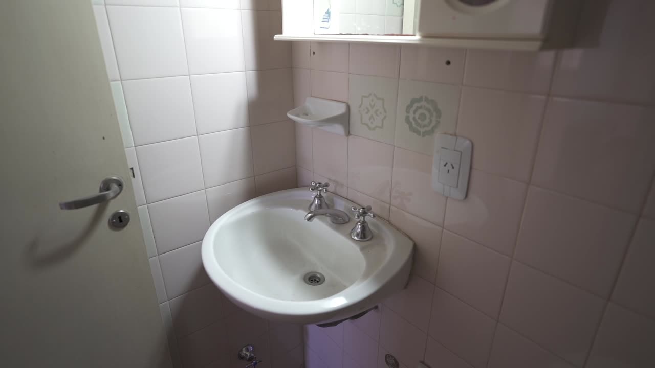 Serene, slow, close up clip captures all-white bathroom with ceramic walls, highlighting sink, mirror, and door. Ideal for Airbnb listings or modern design content.