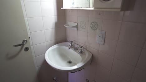 serene, slow, close up clip captures all-white bathroom with ceramic walls, highlighting sink, mirror, and door. ideal for airbnb listings or modern design content.