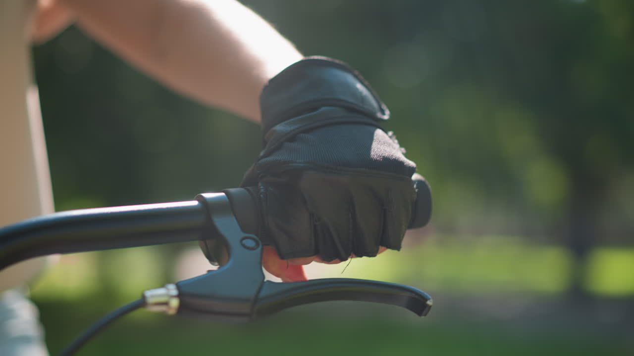 primer plano del manillar de la bicicleta individual con la mano con guantes, acelerando y sosteniendo el freno, la luz del sol se refleja en la mano, con vegetación suavemente borrosa en el fondo