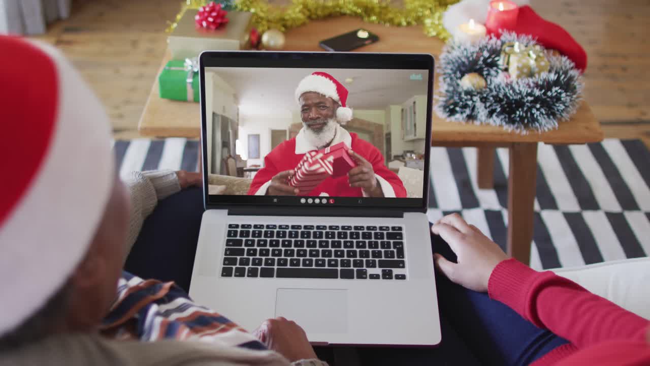 madre y hija afroamericanas usando una computadora portátil para una videollamada de navidad con santa en la pantalla