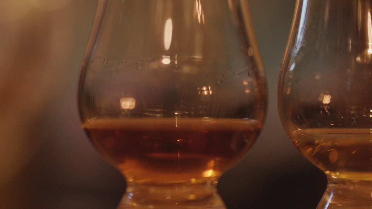 Close-up of whisky glasses with amber liquid, candlelight reflections, and cozy night ambiance