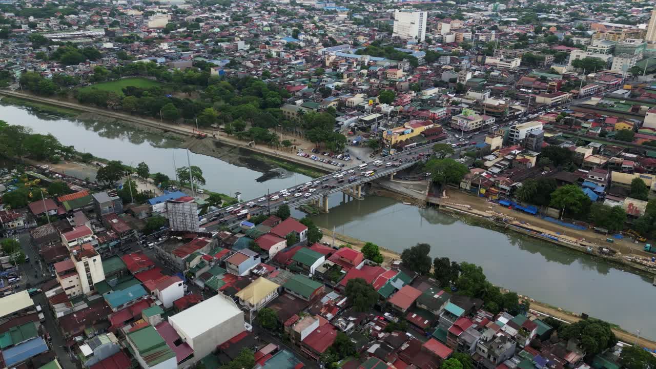 Cars cross bridge over river with dense city housing on both sides in Marikina, Metro Manila, Philippines at rush hour