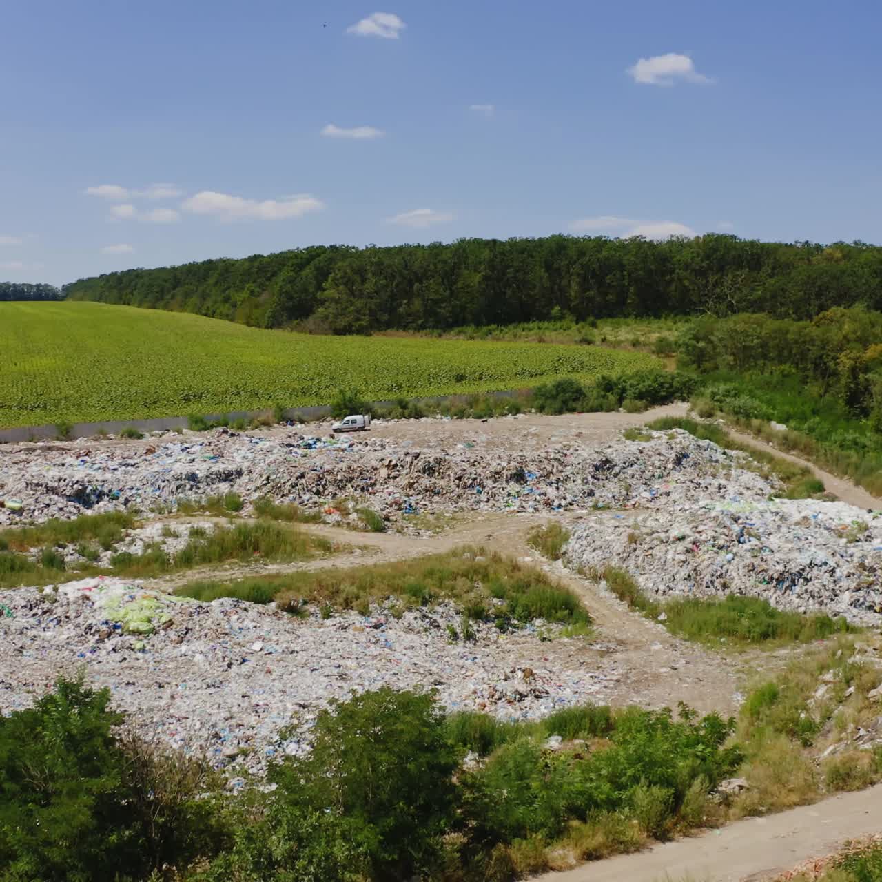 Garbage among nature. Piles of rubbish on field surrounded by green trees. Pollution of environment. Dirty litter in summer. Aerial view.