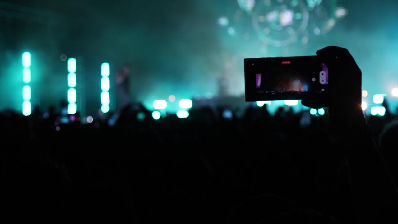 Atmosfera vibrante: i fan filmano la performance dal vivo del cantante su un palco illuminato tra luci colorate