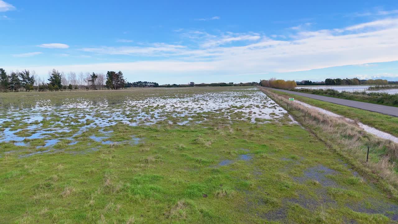 Aerial view of flooded fields under clear skies in Christchurch, showcasing waterlogged landscapes and rural roads