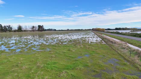 aerial view of flooded fields under clear skies in christchurch, showcasing waterlogged landscapes and rural roads