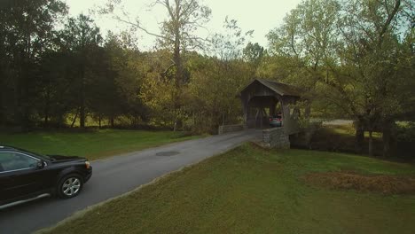 a white car and a dark sport utility vehicle drive through a covered bridge in rural tennessee