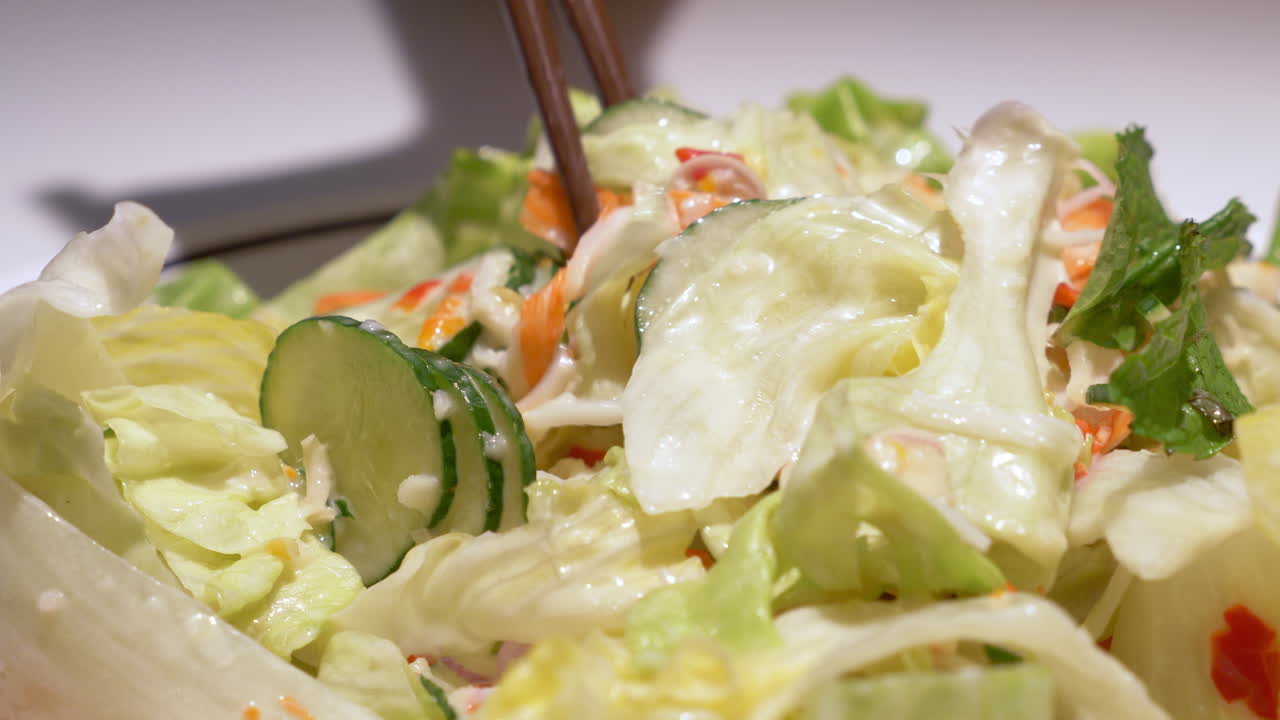 Picking some vegetables using a pair of chopsticks from a bowl filled with vegetables, drizzled with salad dressing