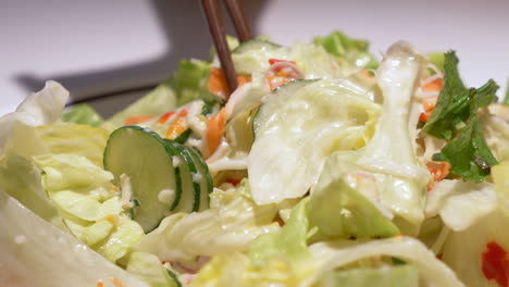 picking some vegetables using a pair of chopsticks from a bowl filled with vegetables, drizzled with salad dressing