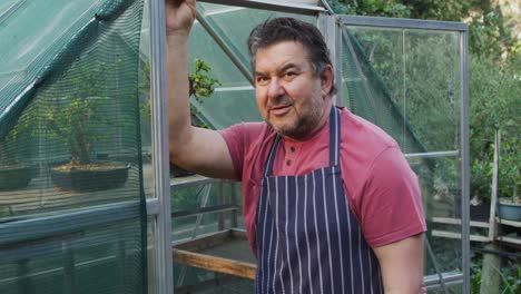 Caucasian-male-gardener-standing-at-greenhouse,-looking-at-camera-and-smiling-at-garden-center