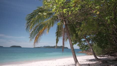 Imágenes-Inclinadas-Hacia-Abajo-De-Una-Playa-De-Arena-Blanca-Con-Aguas-Turquesas,-Palmeras-E-Islas-A-Lo-Lejos