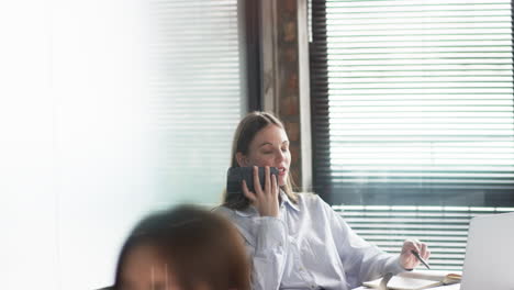 Young-Caucasian-businesswoman-in-a-striped-shirt-uses-a-smartphone-in-an-office-setting