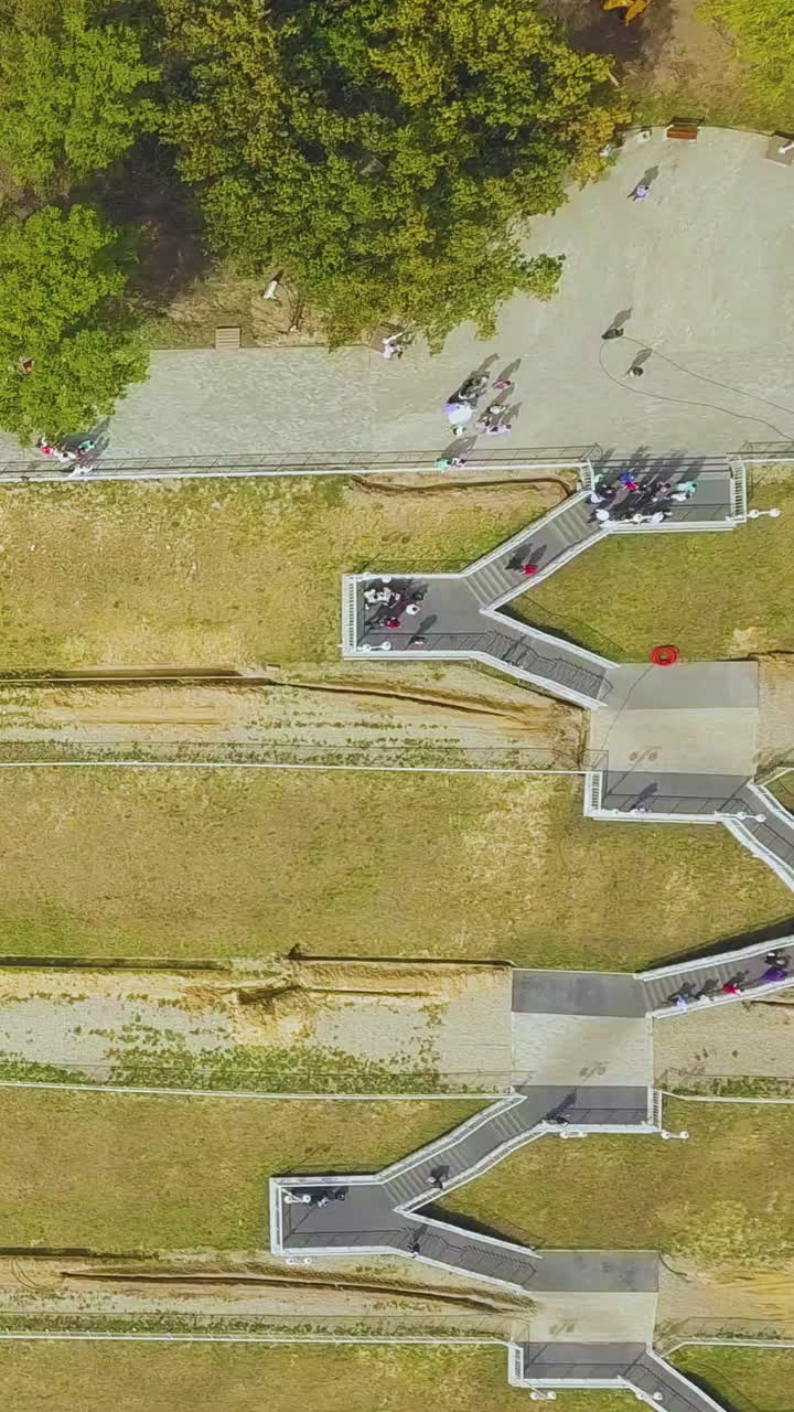 newlywed couple in park on green hilly embankment with modern overpass stairs on warm autumn day upper view