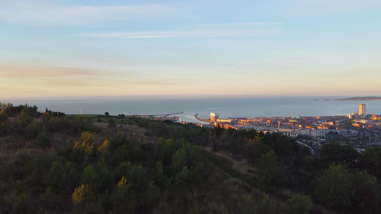 vista aérea ascendente de las colinas y la ciudad al amanecer con edificios y puerto deportivo