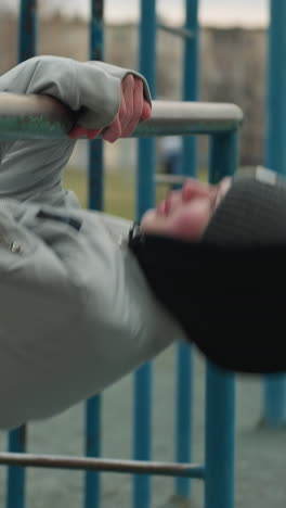 close-up of a young boy exercising on an iron bar in the stadium, he is wearing a gray jacket and beanie