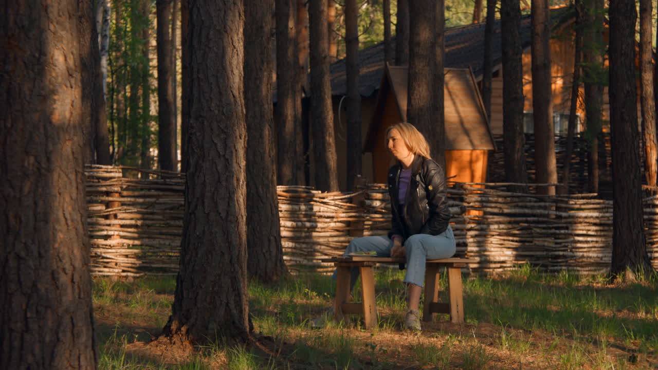 mujer almorzando en un bosque cerca de una cabaña