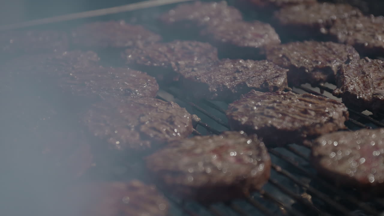 Hamburger su barbecue a carbone untuoso e fumoso in un pomeriggio estivo su griglia commerciale al rallentatore