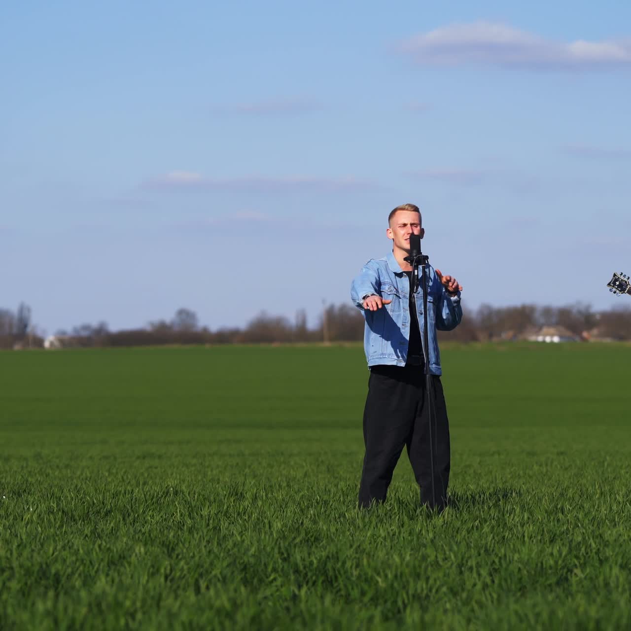 Guitarist, drummer and singer make performance among the fields. Young men musicians play music in the nature backdrop