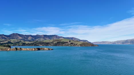 aerial footage captures akaroa's stunning coastline with clear skies, turquoise waters, and mountainous backdrop in bright daylight