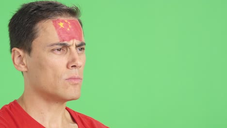 man with chinese flag painted looking away with serious expression