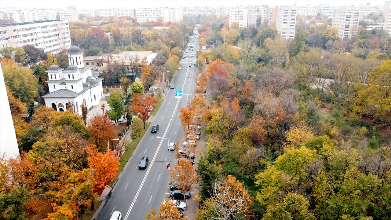 The Titan park with multiple multicolored trees, road with moving cars. Residential buildings and a church near the park. View from the drone, Bucharest, Romania