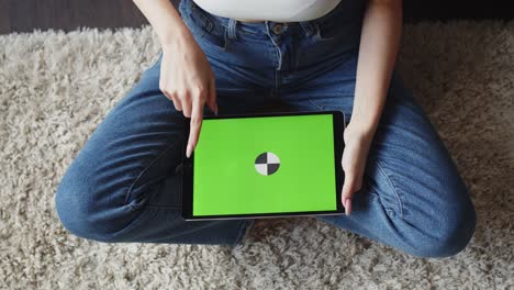 mujer se sienta en el suelo y desliza su dedo sobre la pantalla chromakey de la tableta, vista superior. mujer utiliza tableta digital con pantalla verde, ella desliza con su dedo