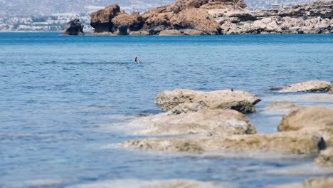 Eine-Person-Schnorchelt-In-Einer-Blauen-Bucht,-Lagune-Am-Mittelmeer,-Windiges-Und-Sonniges-Wetter,-Felsige-Küste,-Mit-Bergen-Im-Hintergrund,-Zypern,-Paphos,-Am-Ende-Eines-Leuchtend-Roten-Schnorchelrohrs