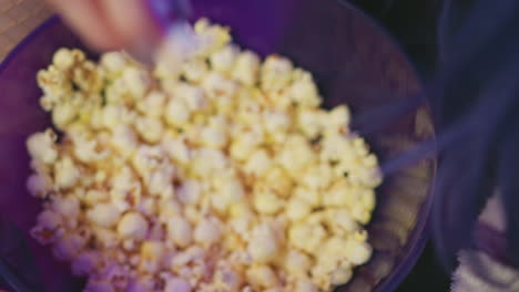 close up of hand reaching into bowl filled with freshly popped popcorn under soft purple ambient light, capturing relaxed moment of casual snacking in cozy indoor