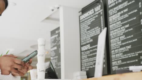 una mujer biracial feliz escaneando un código qr con un teléfono inteligente en un café.