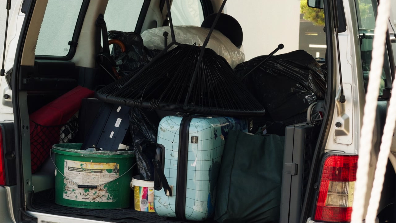 Open car trunk packed with old household items, bags and luggage ready for disposal. Shows decluttering, moving, cleanup and waste removal.