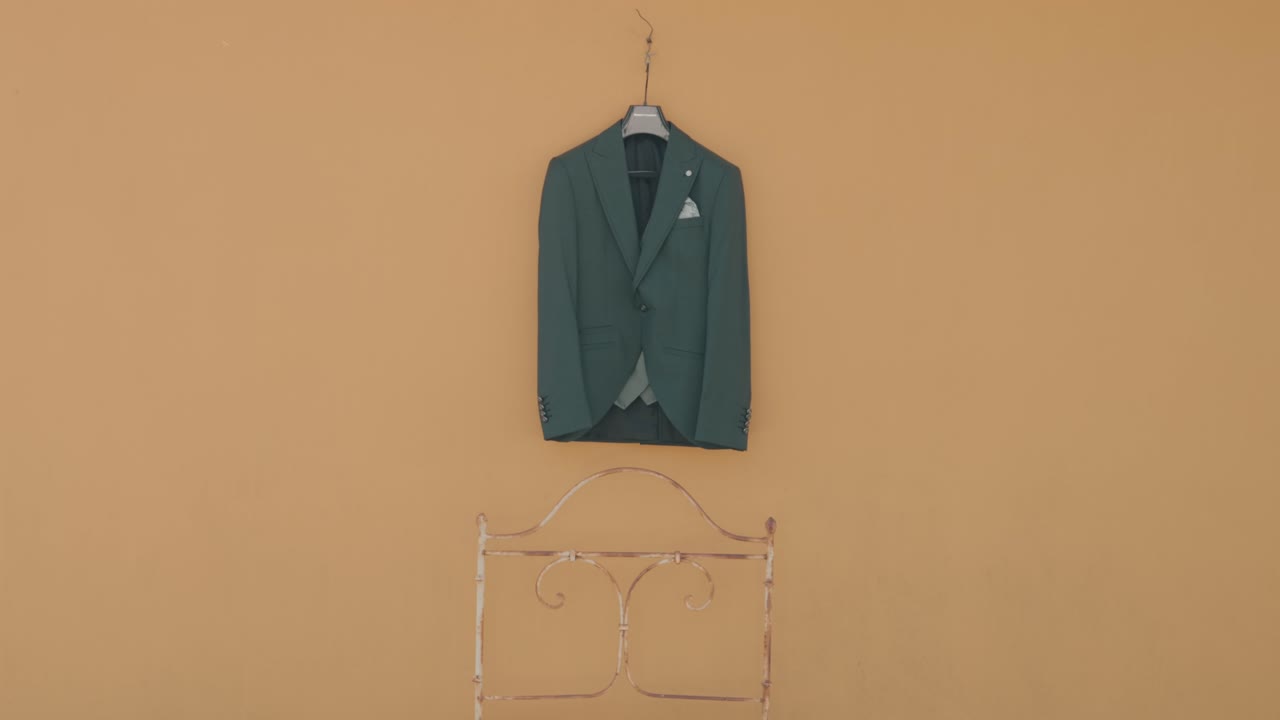 Elegant groom suit displayed on a hanger against a soft yellow wall above a decorative frame