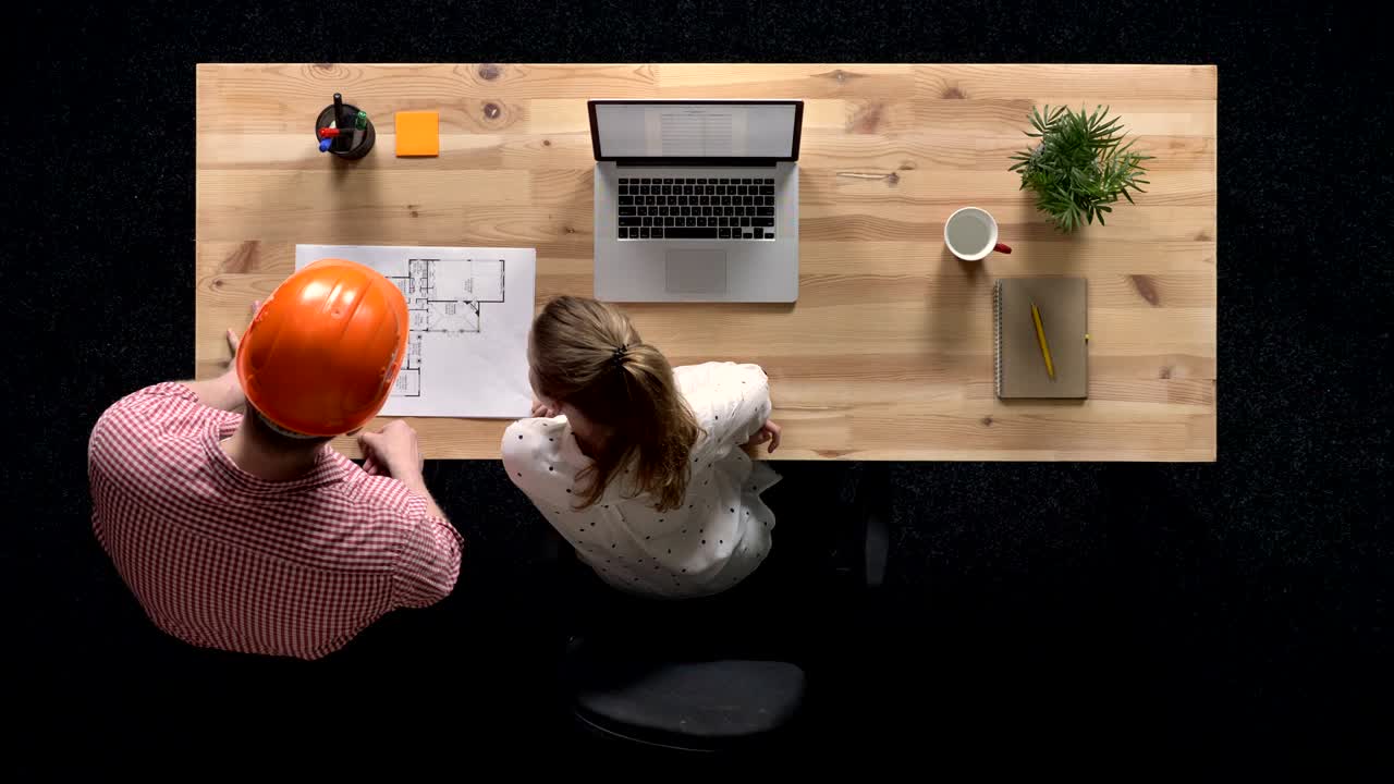 Young businesswoman is working on laptop in daytime, builder comes and shows plan of building, work concept, office concept, communication concept, top shot