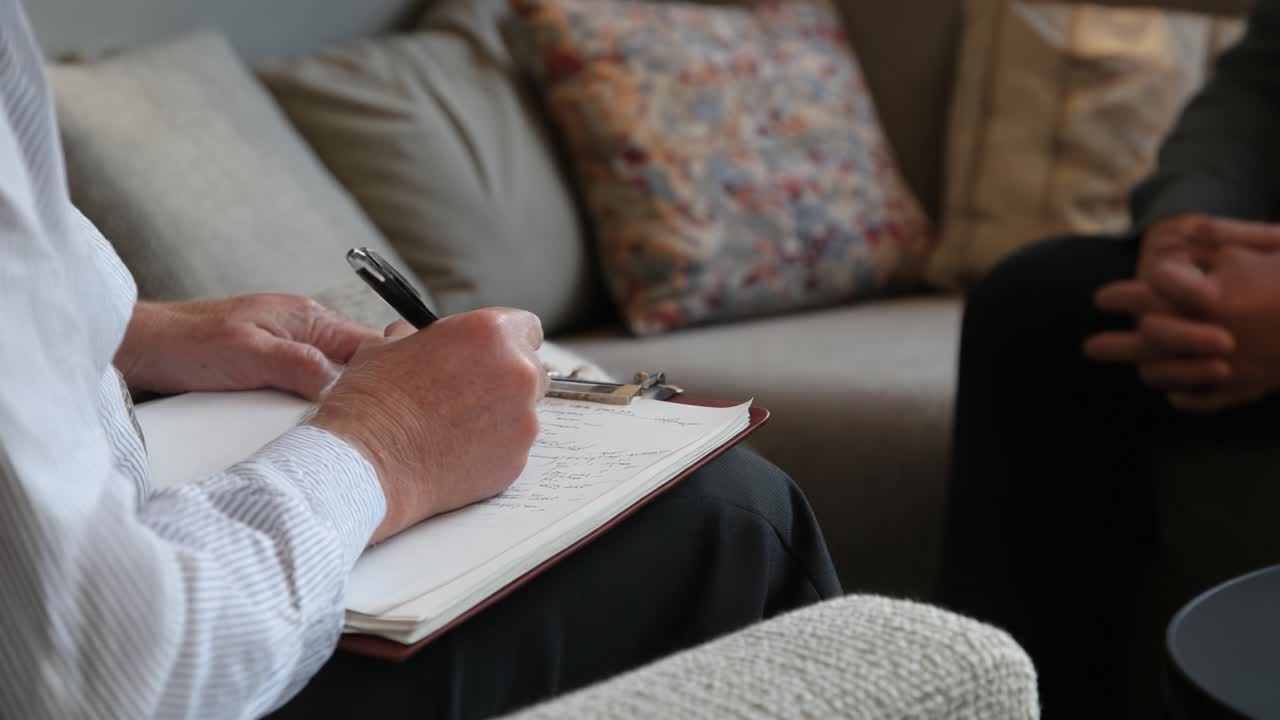 A Reflective Moment of Note-Taking During a Serious Discussion on a Comfortable Sofa, Capturing the Intent and Focus of the Engaged Participants