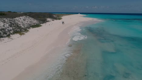una pareja joven camina por la playa de arena blanca desde atrás, una muñeca aérea en un impresionante fondo caribeño