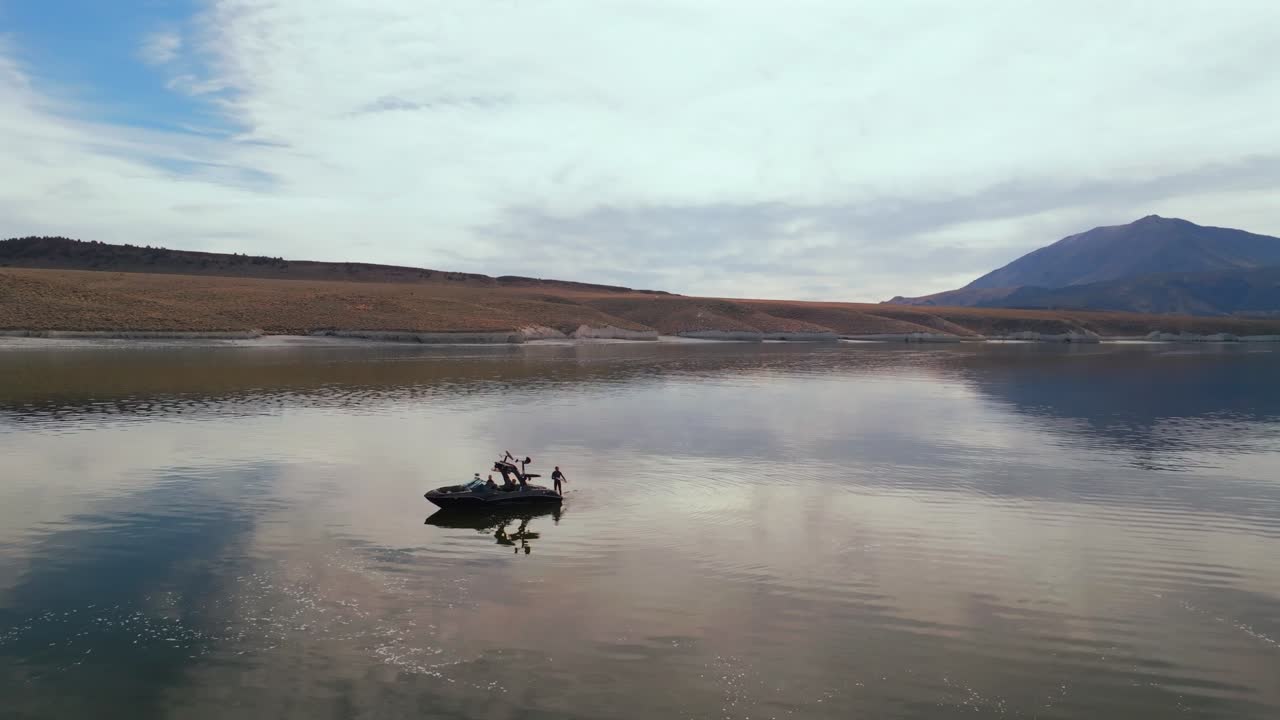 Lake Crowley Mammoth Lakes California aerial drone wake surfer surfing standing on deck back of boat water sports MB boat golden calm water morning sun clouds circle left motion
