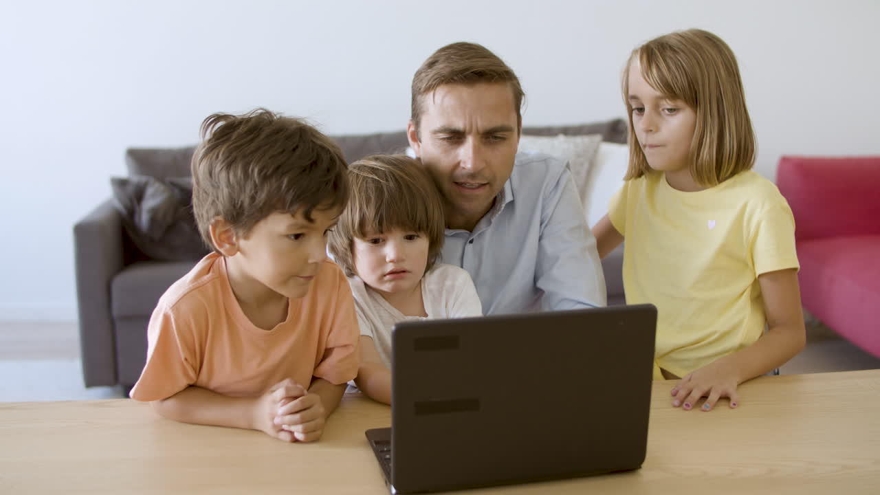 padre caucásico viendo una película a través de una computadora portátil con los niños