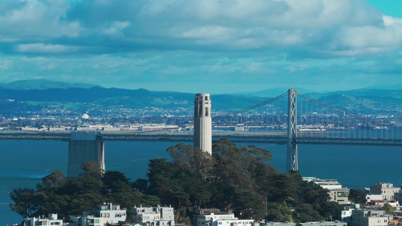 Scatto aereo con teleobiettivo e panning a parallasse della Coit Tower con il Bay Bridge sullo sfondo, in una giornata da cartolina a San Francisco, California. 4K