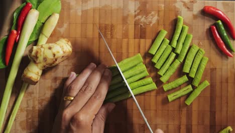 Chopping-and-preparing-green-beans-on-a-bamboo-chopping-board-and-moving-the-pieces-aside---Close-up,-overhead-view